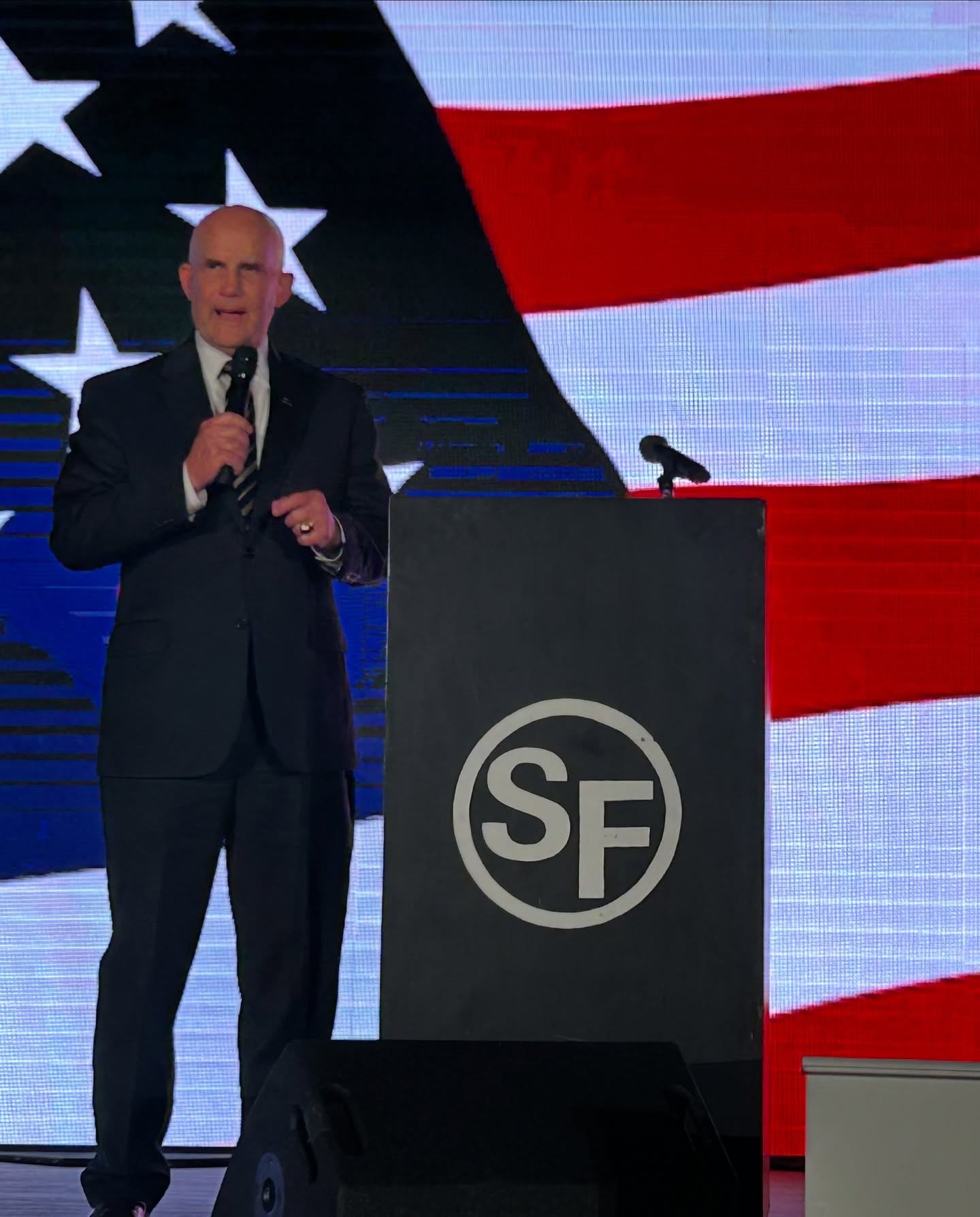 Keith Self addressing supporters before an American flag backdrop